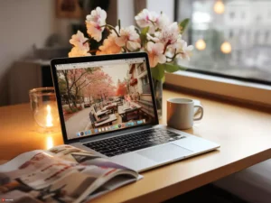 a laptop with a coffee mug on a table near window